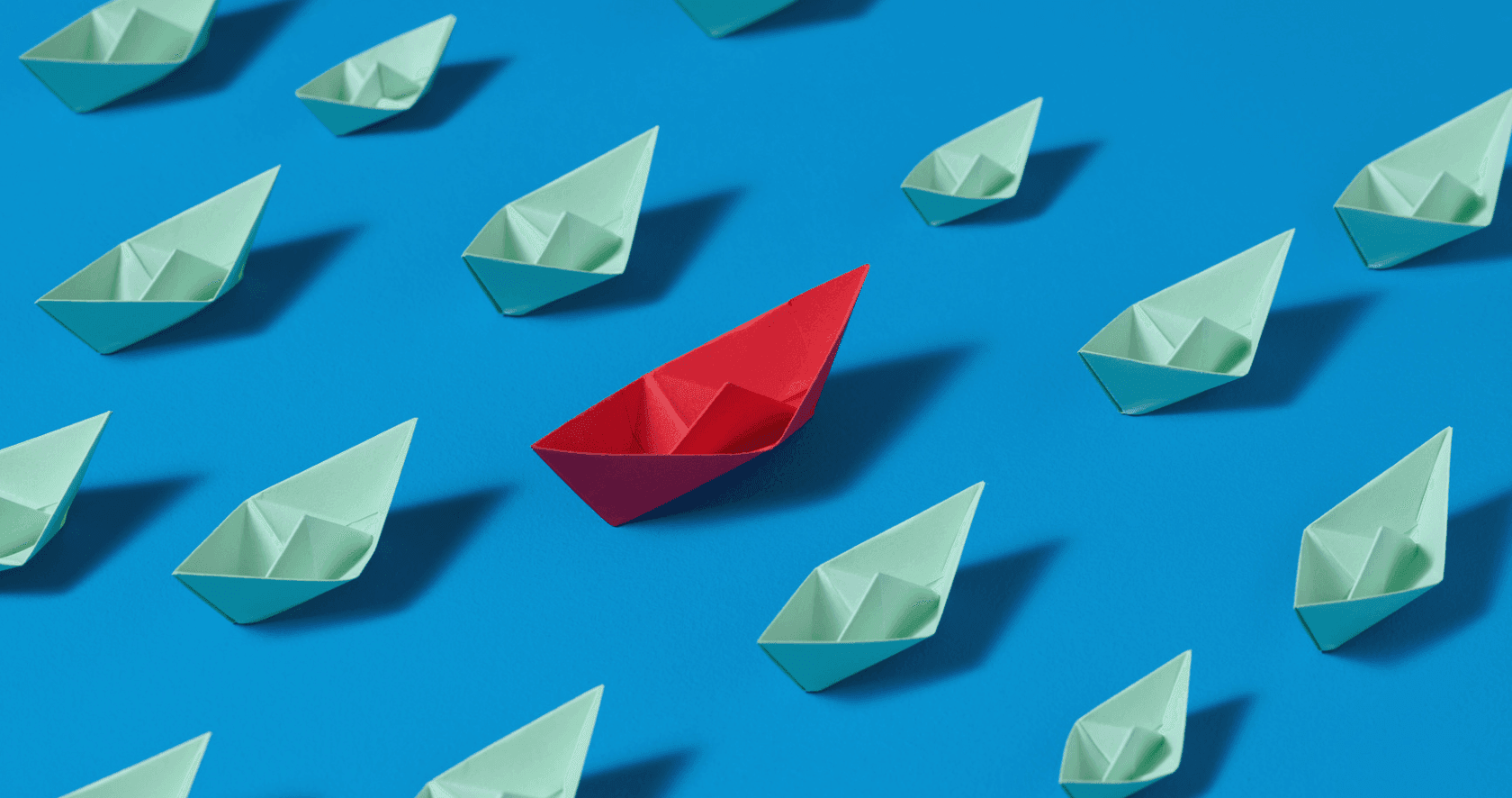 Un bateau en papier rouge se distingue des autres bateaux en papier blancs.